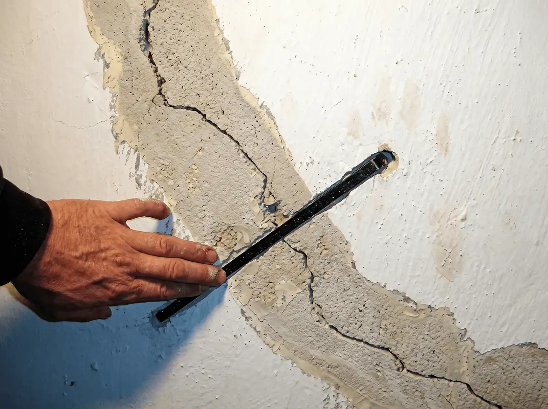 A wall with a large crack is being inspected by a professional in Tuscaloosa, AL