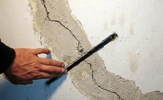 A wall with a large crack is being inspected by a professional in Tuscaloosa, AL